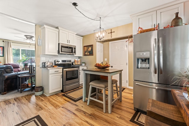 kitchen with ceiling fan with notable chandelier, light hardwood / wood-style flooring, decorative light fixtures, white cabinetry, and stainless steel appliances