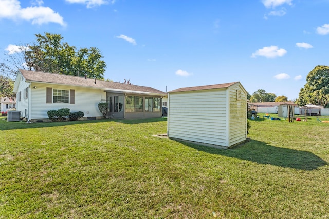 rear view of property featuring a sunroom, a storage unit, a yard, and central AC