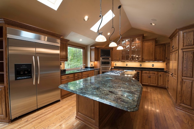 kitchen with sink, light hardwood / wood-style flooring, lofted ceiling with skylight, a kitchen island, and appliances with stainless steel finishes