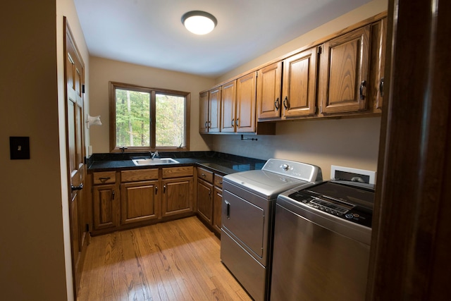 clothes washing area with independent washer and dryer, cabinets, light wood-type flooring, and sink