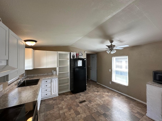 kitchen featuring white cabinets, black fridge, sink, vaulted ceiling, and a textured ceiling