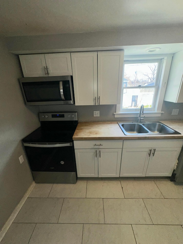 kitchen with butcher block counters, sink, light tile patterned flooring, white cabinets, and appliances with stainless steel finishes