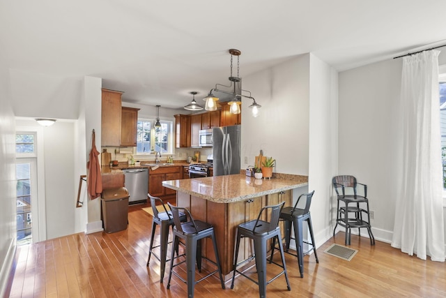 kitchen with a kitchen breakfast bar, hanging light fixtures, light wood-type flooring, appliances with stainless steel finishes, and kitchen peninsula