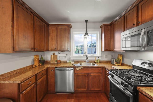 kitchen featuring sink, hanging light fixtures, dark stone countertops, dark hardwood / wood-style flooring, and stainless steel appliances