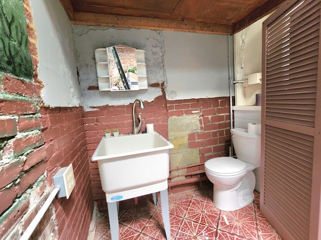 bathroom featuring wooden ceiling, tile patterned flooring, brick wall, and toilet