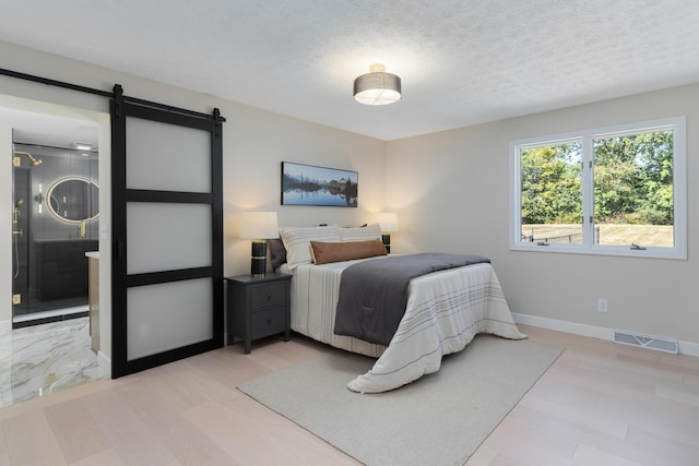 bedroom with a textured ceiling, light hardwood / wood-style flooring, and a barn door