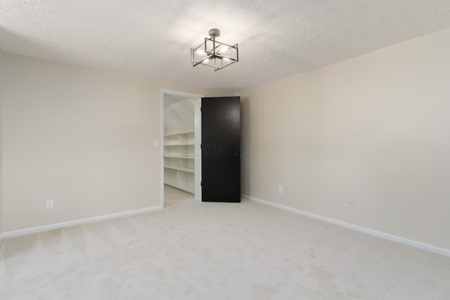 carpeted empty room with a chandelier and a textured ceiling