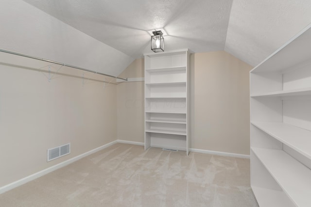 walk in closet with light carpet and vaulted ceiling