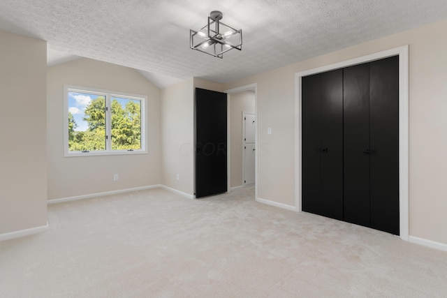 unfurnished bedroom with an inviting chandelier, light colored carpet, lofted ceiling, a textured ceiling, and a closet