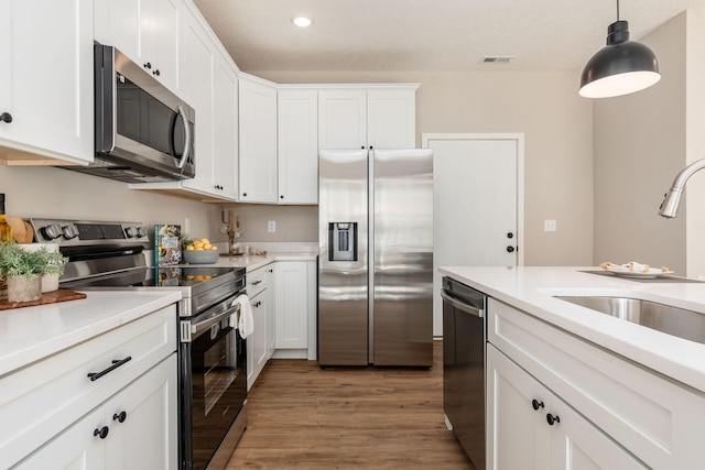 kitchen with white cabinets, appliances with stainless steel finishes, light wood-type flooring, and decorative light fixtures