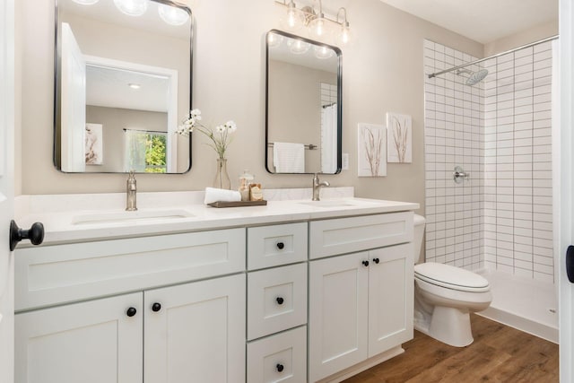 bathroom featuring hardwood / wood-style flooring, vanity, toilet, and tiled shower