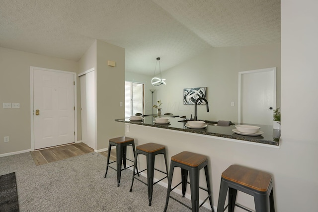 kitchen featuring vaulted ceiling, hardwood / wood-style flooring, decorative light fixtures, a kitchen bar, and kitchen peninsula