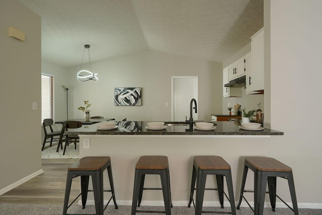 kitchen with white cabinetry, hanging light fixtures, dark hardwood / wood-style flooring, kitchen peninsula, and a breakfast bar