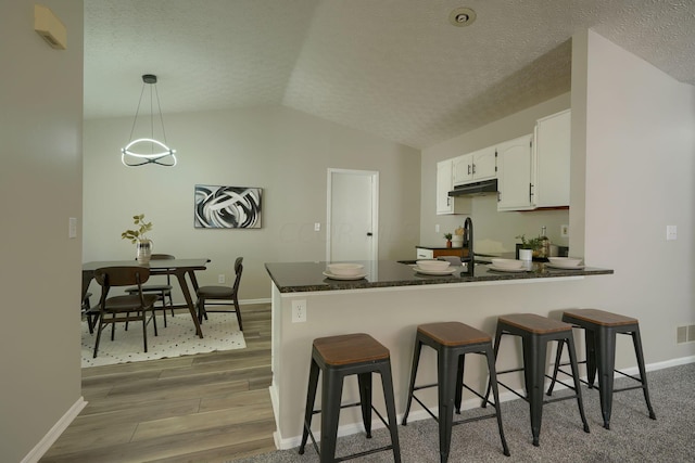 kitchen with hanging light fixtures, kitchen peninsula, lofted ceiling, white cabinets, and hardwood / wood-style flooring