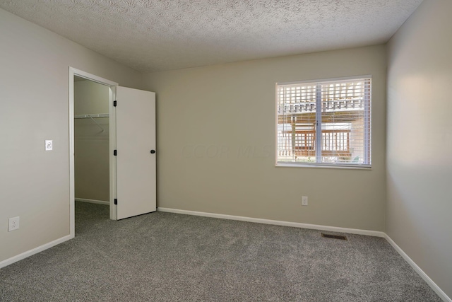 unfurnished bedroom featuring carpet flooring, a textured ceiling, a walk in closet, and a closet