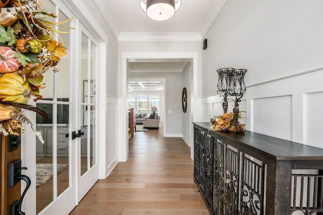 hallway featuring ornamental molding, light wood-type flooring, and french doors