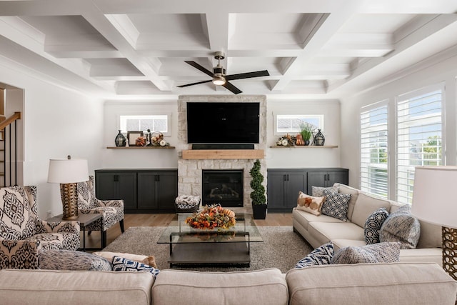 living room featuring coffered ceiling, a stone fireplace, light hardwood / wood-style floors, and beam ceiling