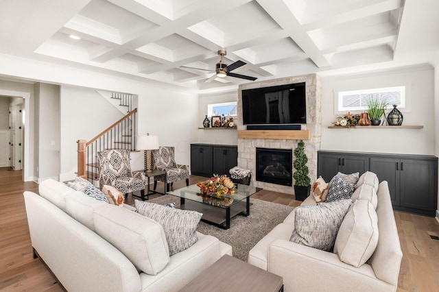 living room featuring beam ceiling, coffered ceiling, a fireplace, and light wood-type flooring