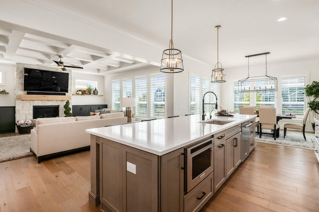 kitchen with pendant lighting, sink, a kitchen island with sink, stainless steel microwave, and light wood-type flooring