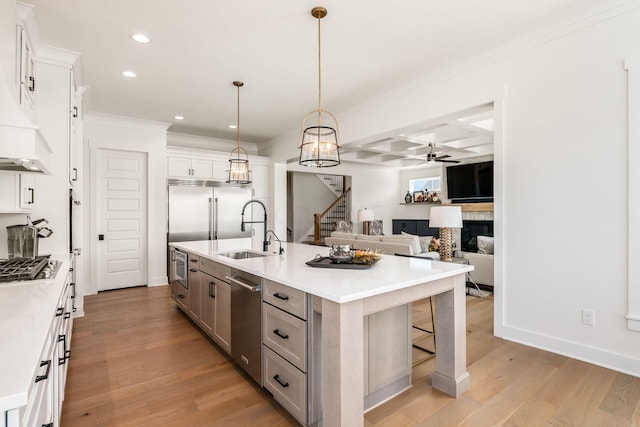 kitchen featuring pendant lighting, white cabinetry, an island with sink, sink, and light wood-type flooring