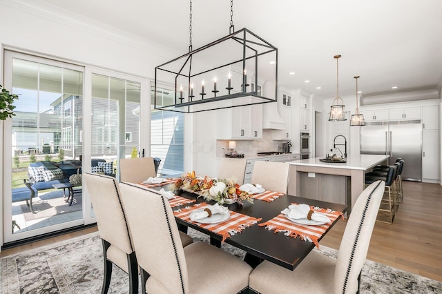 dining space featuring ornamental molding, sink, and light hardwood / wood-style flooring