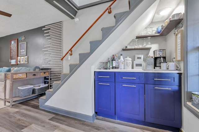 bar with stairs, a bar, a textured ceiling, and light wood-style floors