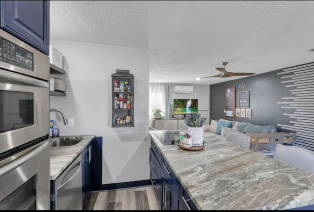 kitchen with a textured ceiling, light wood-style flooring, a sink, blue cabinetry, and appliances with stainless steel finishes