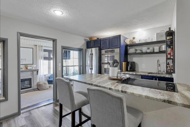 kitchen featuring a glass covered fireplace, a kitchen breakfast bar, blue cabinets, stainless steel appliances, and a sink