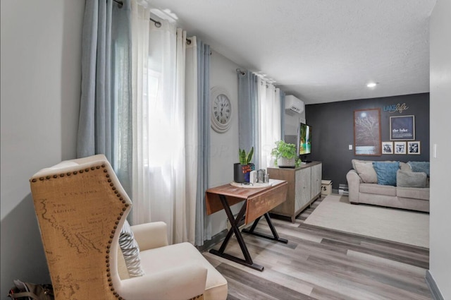 sitting room featuring a textured ceiling, an AC wall unit, and light wood-type flooring