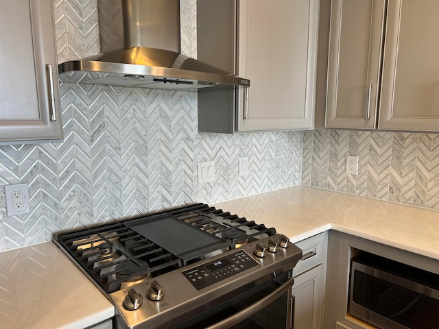 kitchen with gray cabinetry, decorative backsplash, wall chimney range hood, and appliances with stainless steel finishes