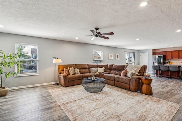 living room featuring hardwood / wood-style flooring, ceiling fan, and a textured ceiling