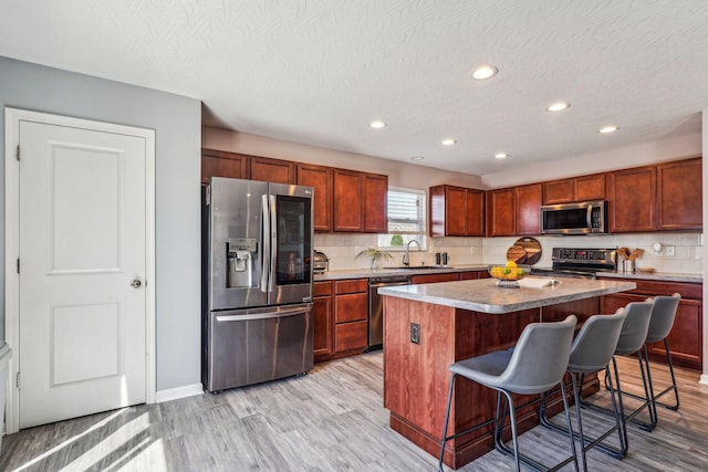 kitchen featuring a kitchen breakfast bar, sink, light hardwood / wood-style floors, appliances with stainless steel finishes, and a kitchen island