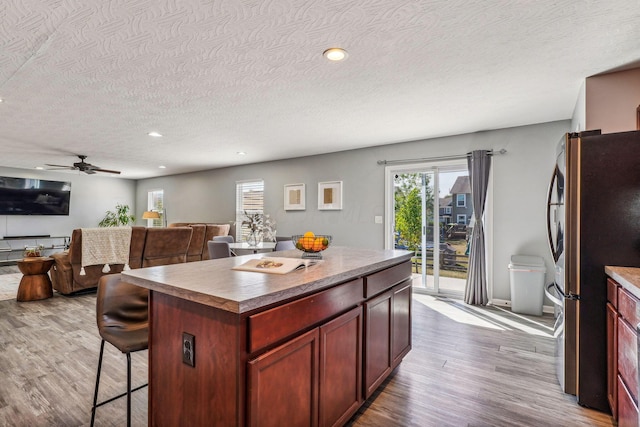 kitchen with stainless steel fridge, a center island, a textured ceiling, and light wood-type flooring