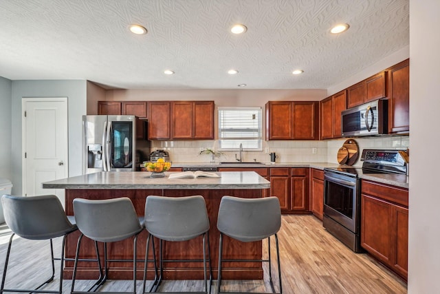 kitchen featuring a kitchen bar, light wood-type flooring, a textured ceiling, stainless steel appliances, and a center island