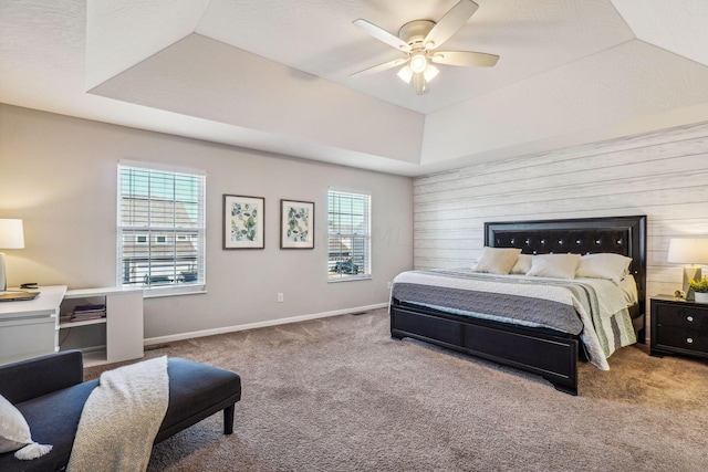 carpeted bedroom featuring ceiling fan, wood walls, and a raised ceiling