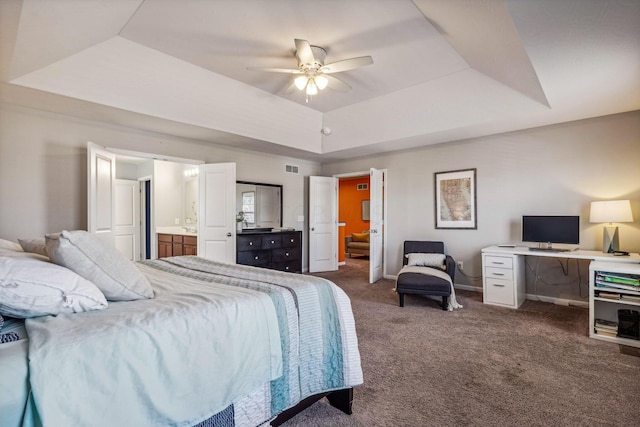 bedroom featuring ceiling fan, dark carpet, connected bathroom, and a tray ceiling