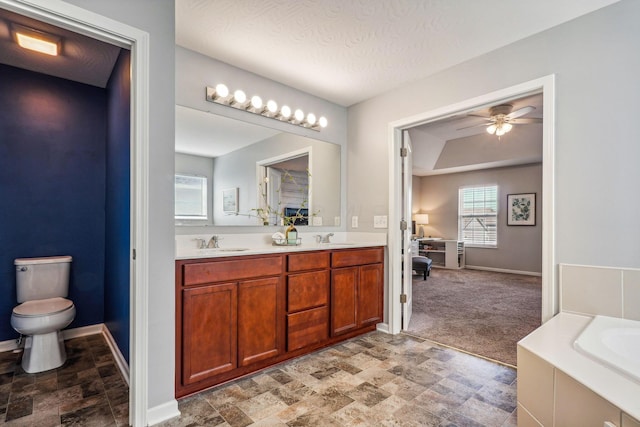 bathroom featuring a textured ceiling, vanity, ceiling fan, toilet, and a bathing tub