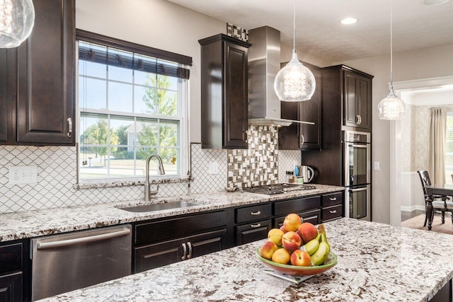 kitchen featuring dark brown cabinetry, stainless steel appliances, wall chimney range hood, sink, and decorative light fixtures