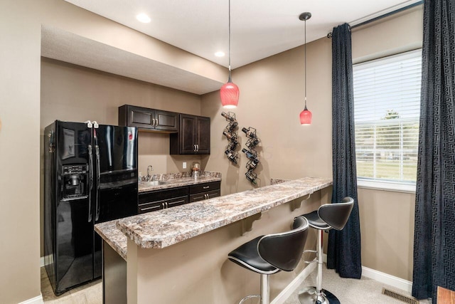 kitchen with kitchen peninsula, black refrigerator with ice dispenser, a breakfast bar, dark brown cabinets, and pendant lighting