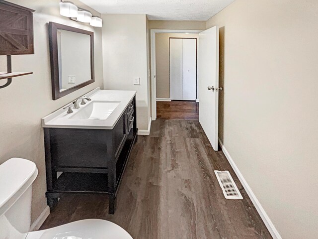 bathroom featuring a textured ceiling, vanity, hardwood / wood-style flooring, and toilet