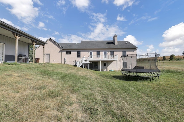 rear view of property with a yard, a trampoline, and a wooden deck