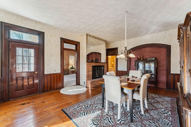 dining room with hardwood / wood-style floors, wooden walls, a fireplace, a textured ceiling, and a notable chandelier