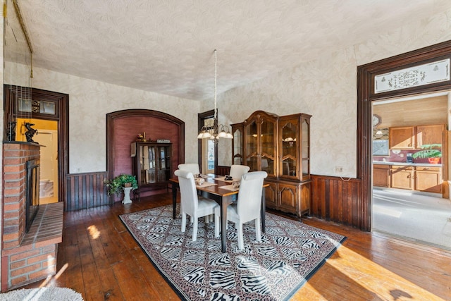 dining space with wooden walls, a fireplace, dark wood-type flooring, and a textured ceiling