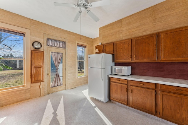 kitchen with ceiling fan, wooden walls, light colored carpet, and white appliances