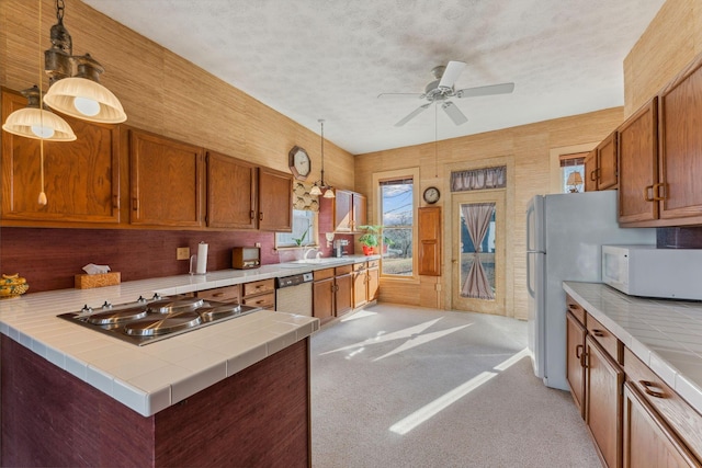 kitchen with light carpet, stainless steel appliances, ceiling fan, decorative light fixtures, and tile countertops