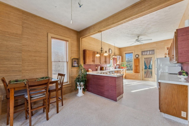 kitchen featuring ceiling fan with notable chandelier, a textured ceiling, decorative light fixtures, light colored carpet, and kitchen peninsula