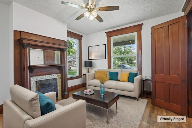 living room featuring ceiling fan, a stone fireplace, light wood-type flooring, and a textured ceiling