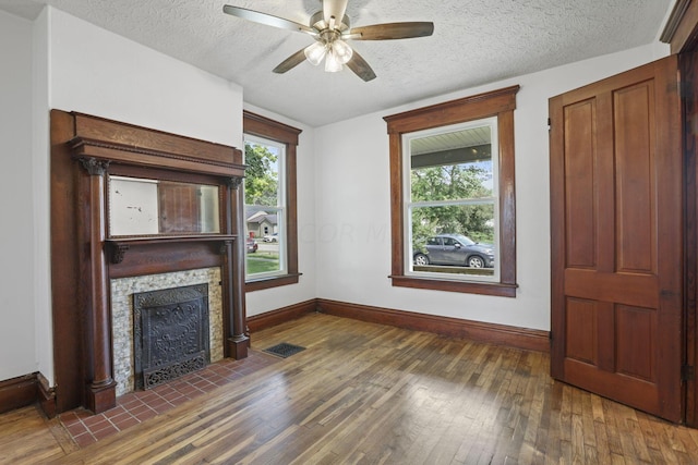 unfurnished living room featuring dark hardwood / wood-style flooring, a textured ceiling, a stone fireplace, and ceiling fan