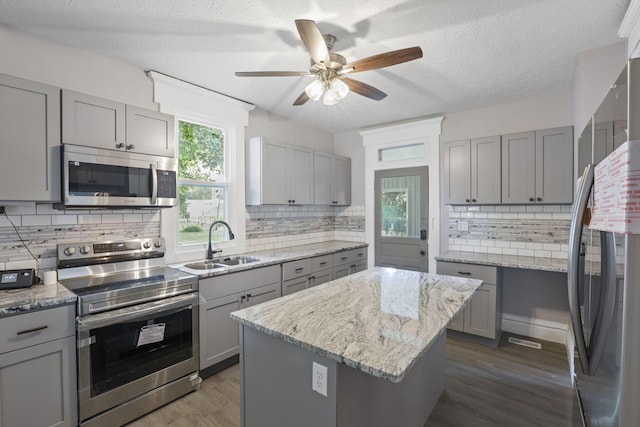 kitchen featuring appliances with stainless steel finishes, a center island, gray cabinets, and sink