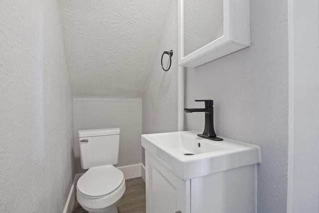 bathroom with hardwood / wood-style floors, vanity, toilet, and vaulted ceiling